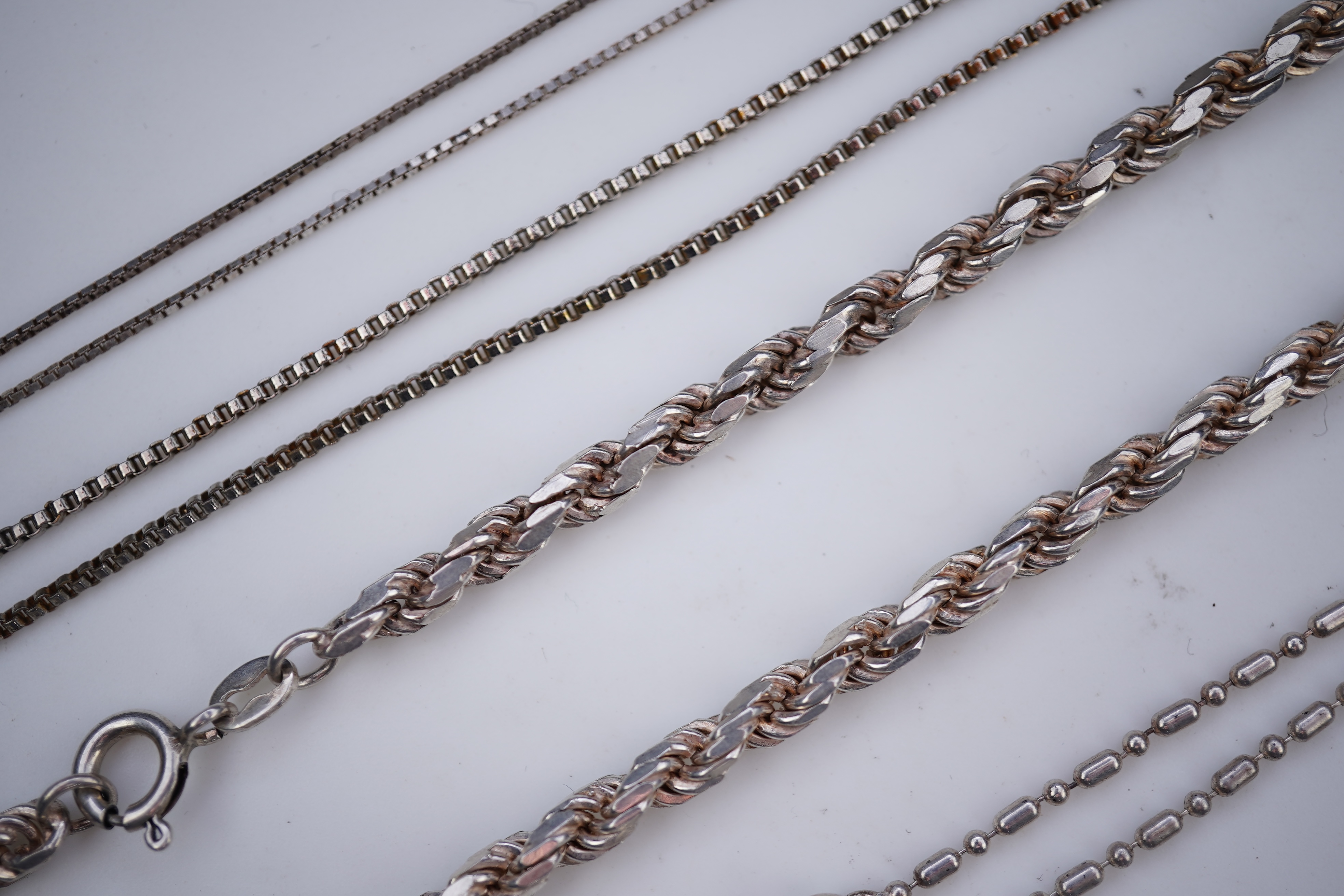 A collection of silver jewels, comprising: a bangle; a chain necklace suspending two winding toothpicks, one with toothpick deficient; a rope twist chain; a pair of cufflinks with the initials DBH; a pendant of abstract